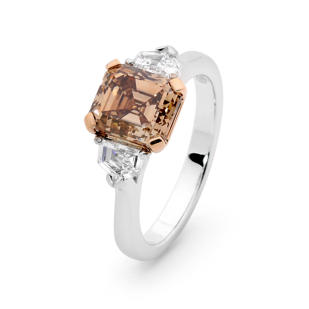 White gold ring with a central Asscher-cut peach champagne diamond flanked by two smaller diamonds on white background