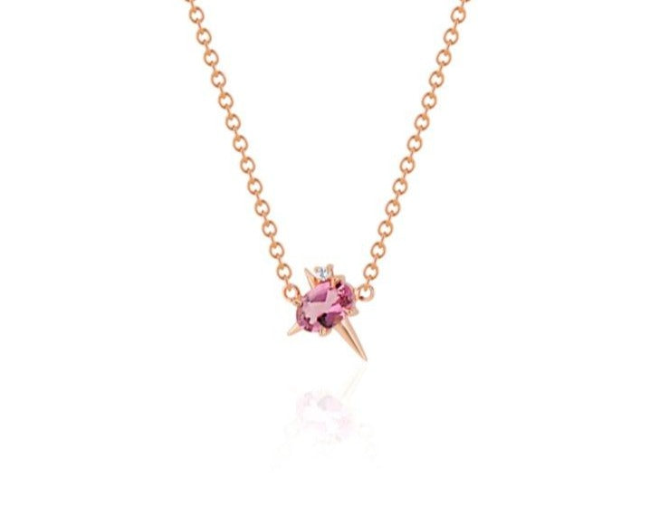 Front view of pendant necklace featuring an oval-shaped pink tourmaline gemstone with small round diamond fixed to a rose gold round-link chain. 2 short spikes extend from top and side with a larger spike angled down, creating an angled crucifix.