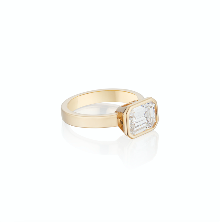 Gold ring with a single emerald cut diamond, isolated on a white background.