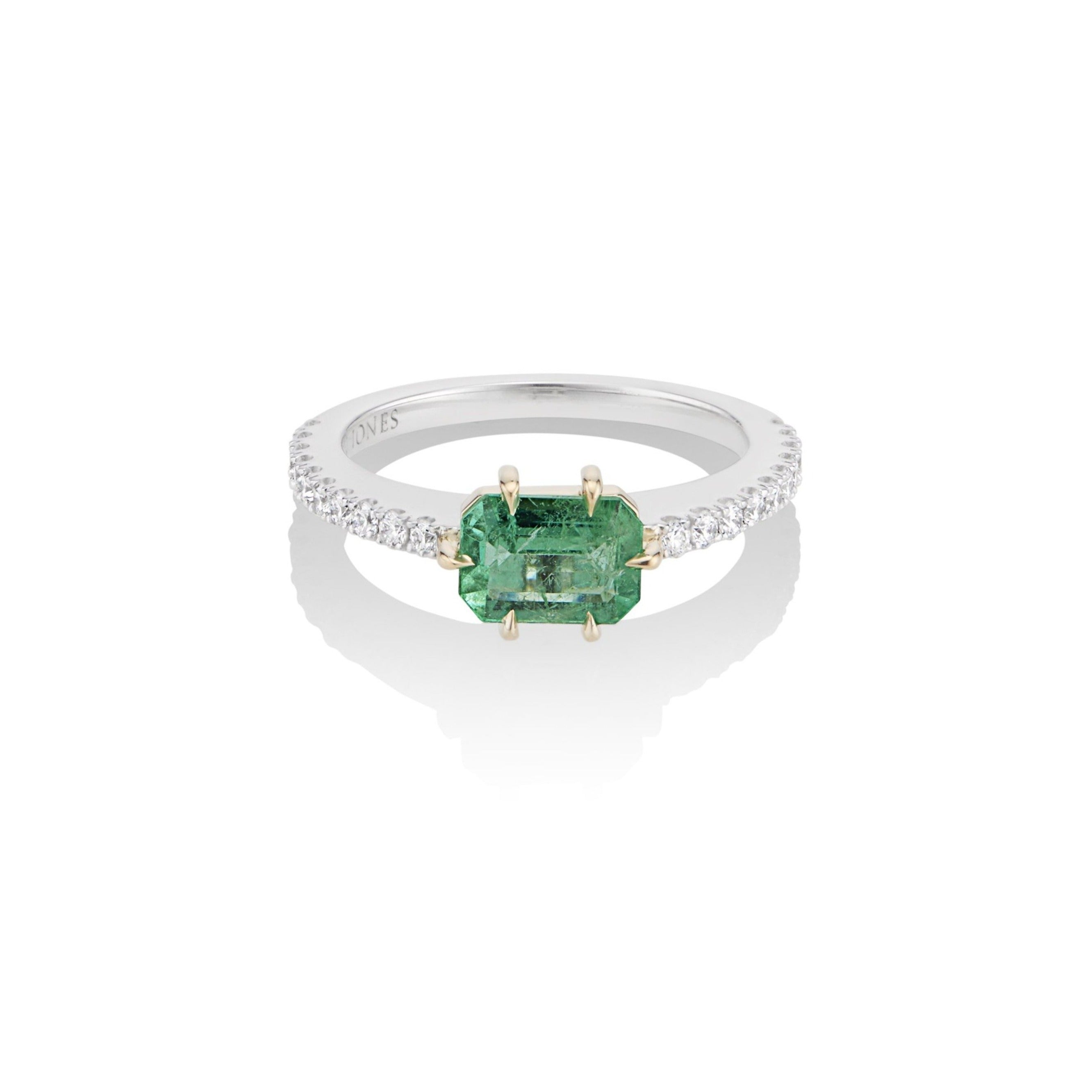 Top view of alternative emerald and diamond engagement ring. The emerald center stone is fixed with a yellow gold 6-prong setting, and mounted atop a U-cut diamond pave band in white gold. The interior band engraving reads, “Harlin Jones.”
