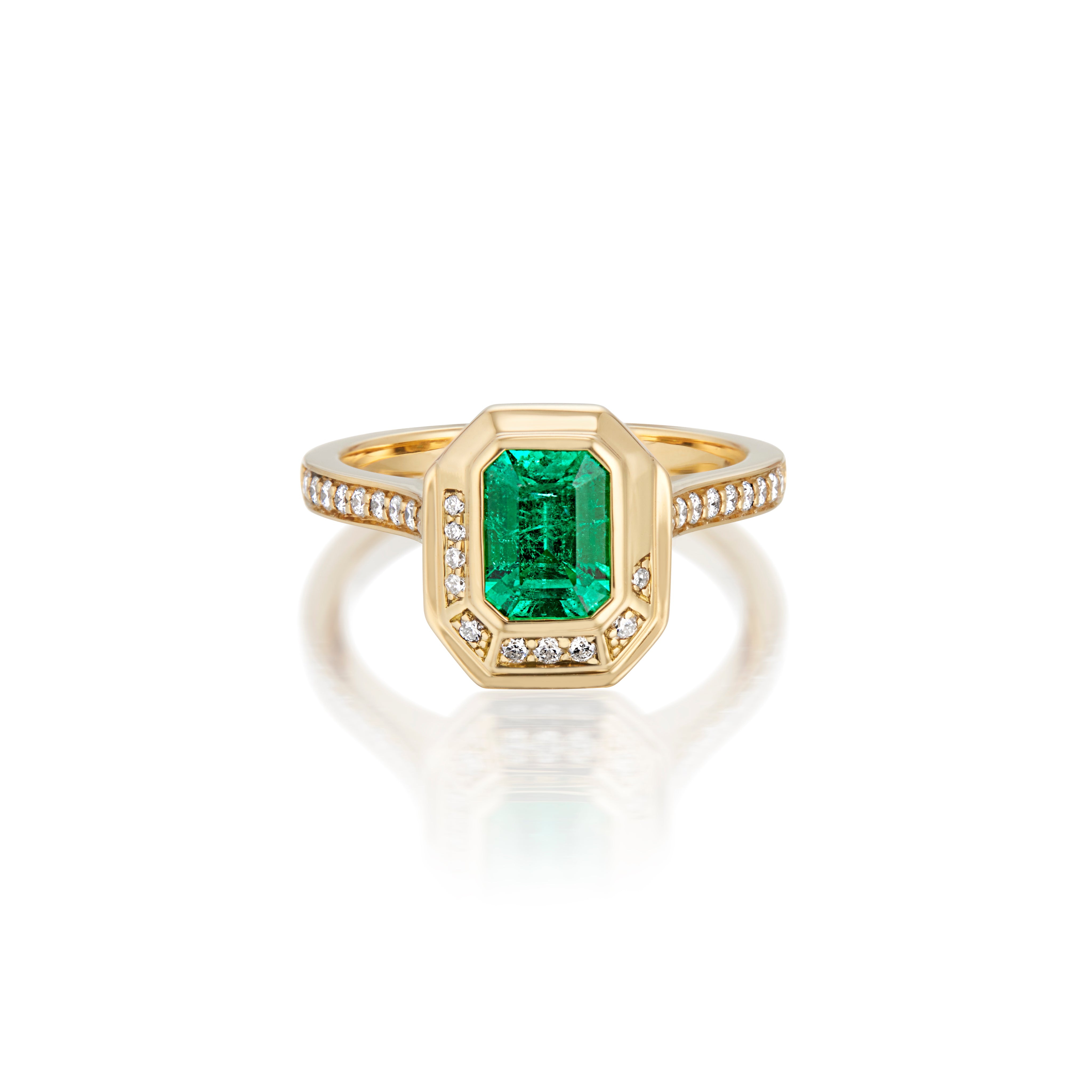 Gold ring with rectangular emerald and diamond accents on a reflective surface.