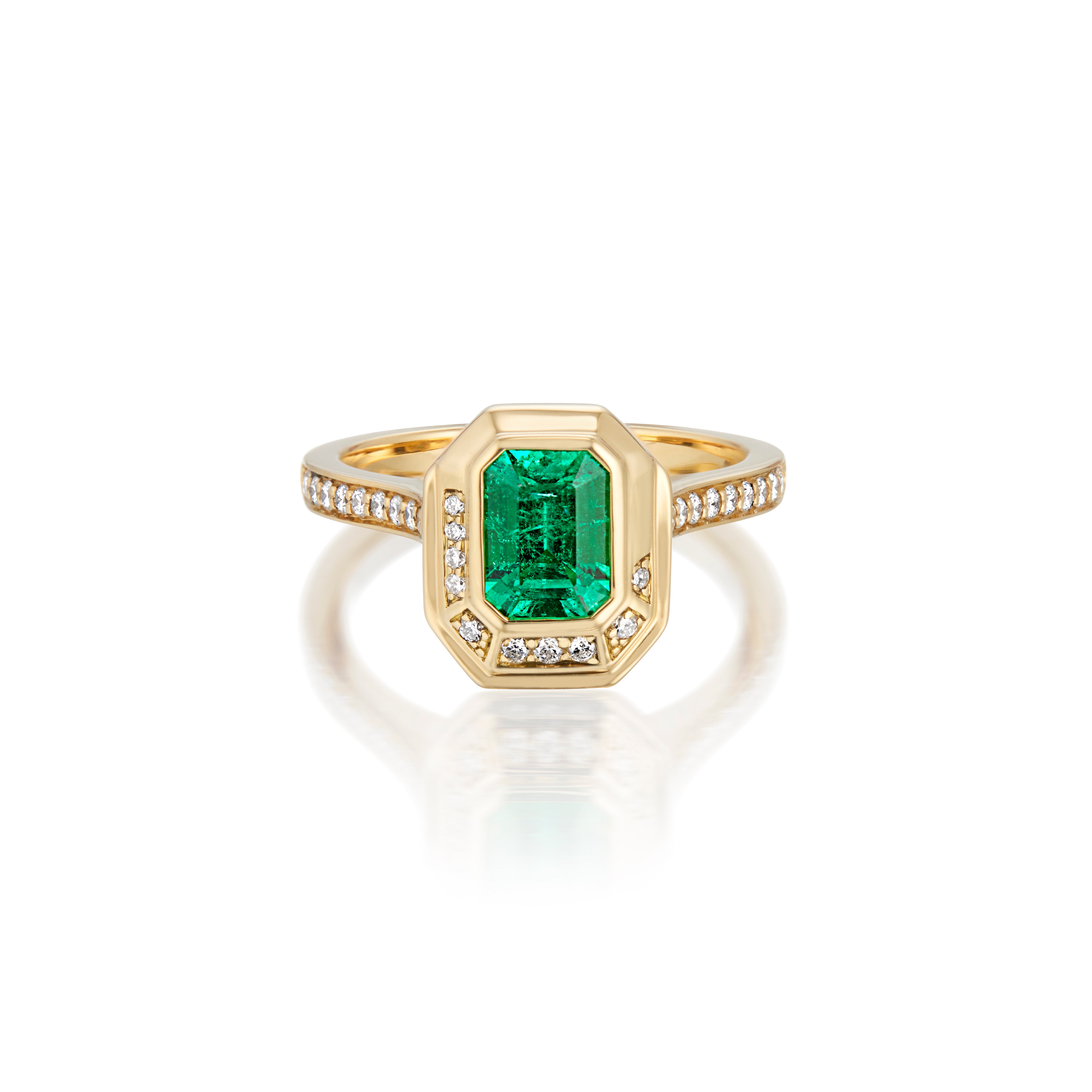 Gold ring with rectangular emerald and diamond accents on a reflective surface.