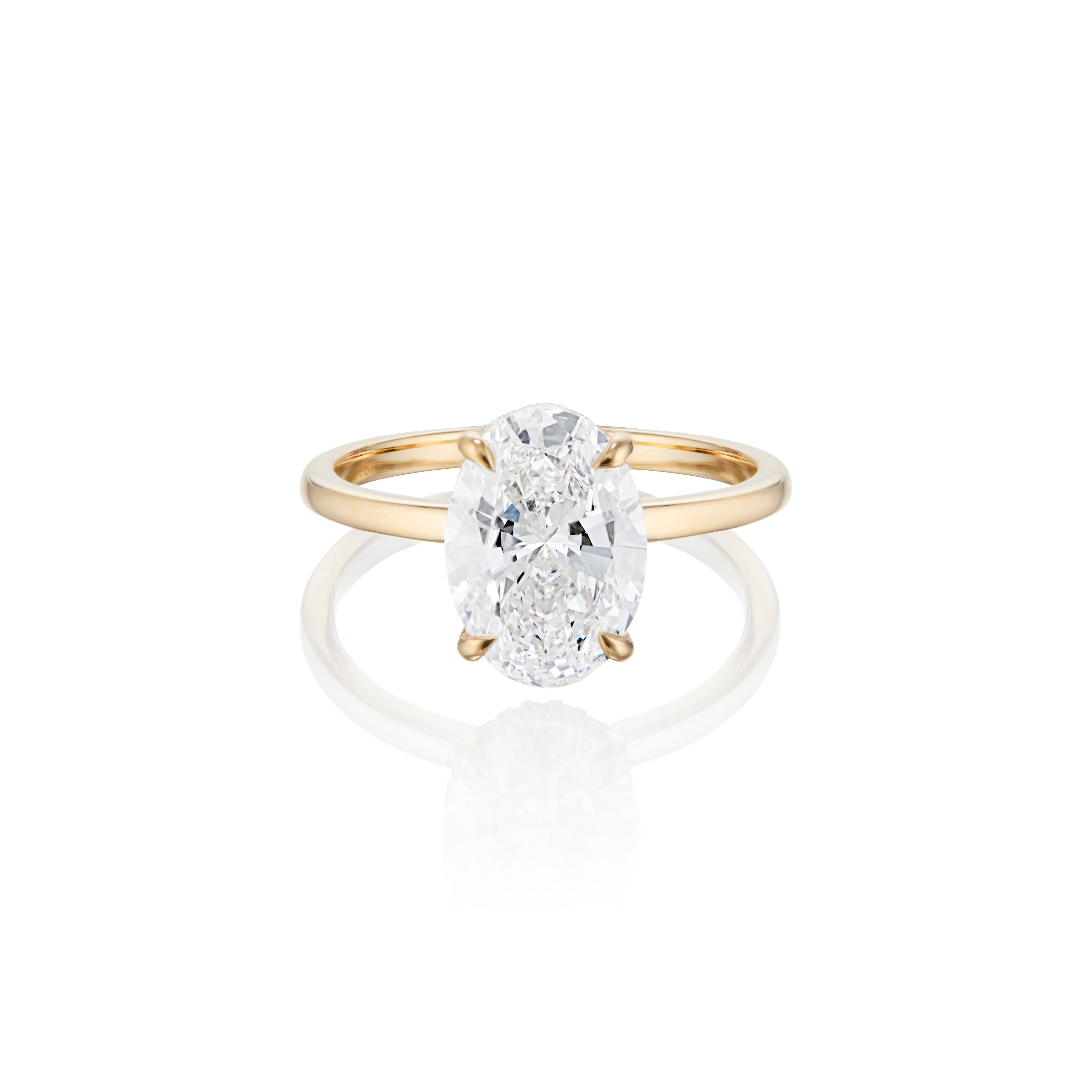 Oval-cut diamond engagement ring on a gold band with a reflective surface below.