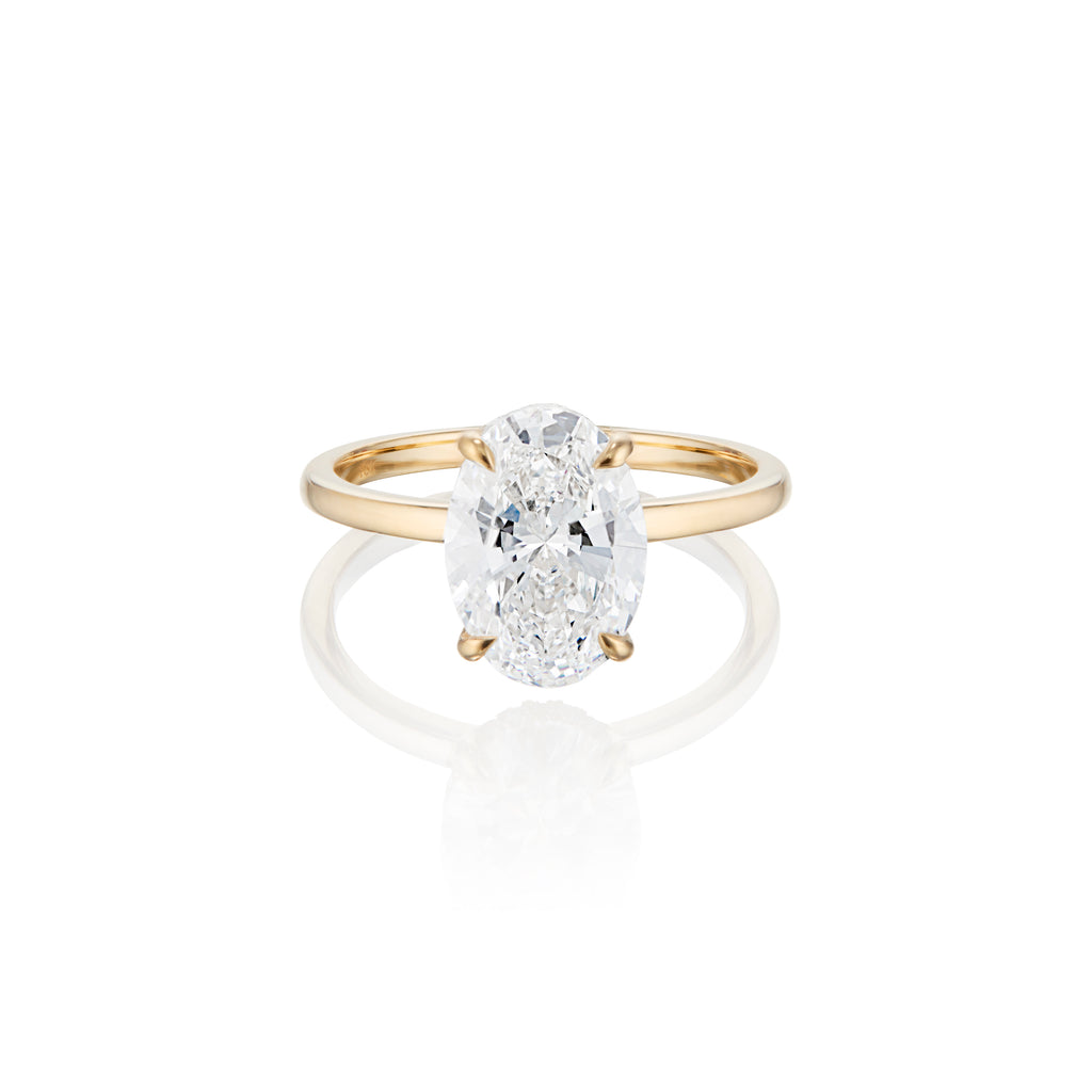 Oval-cut diamond engagement ring on a gold band with a reflective surface below.