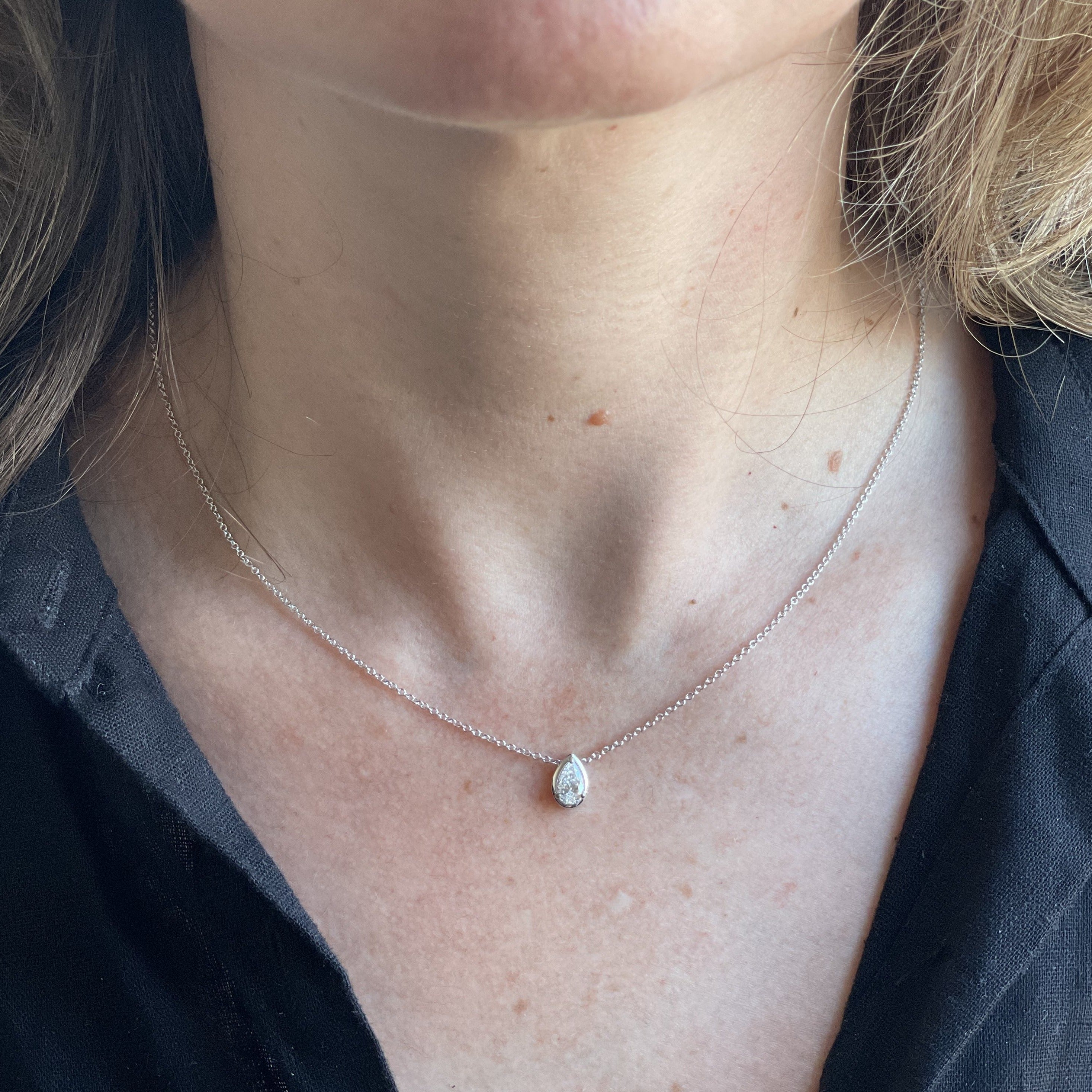 Woman wearing a pear-shaped single solitaire diamond necklace on a thin white-gold chain.