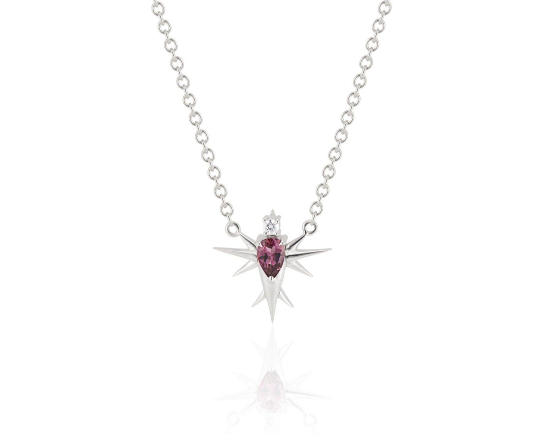 Front view of abstract bird necklace connected to a white gold round-link chain. A pear-shaped pink tourmaline stone forms the bird’s body, topped with a round diamond head. White gold spikes extend from the body to form wings and a tail. 