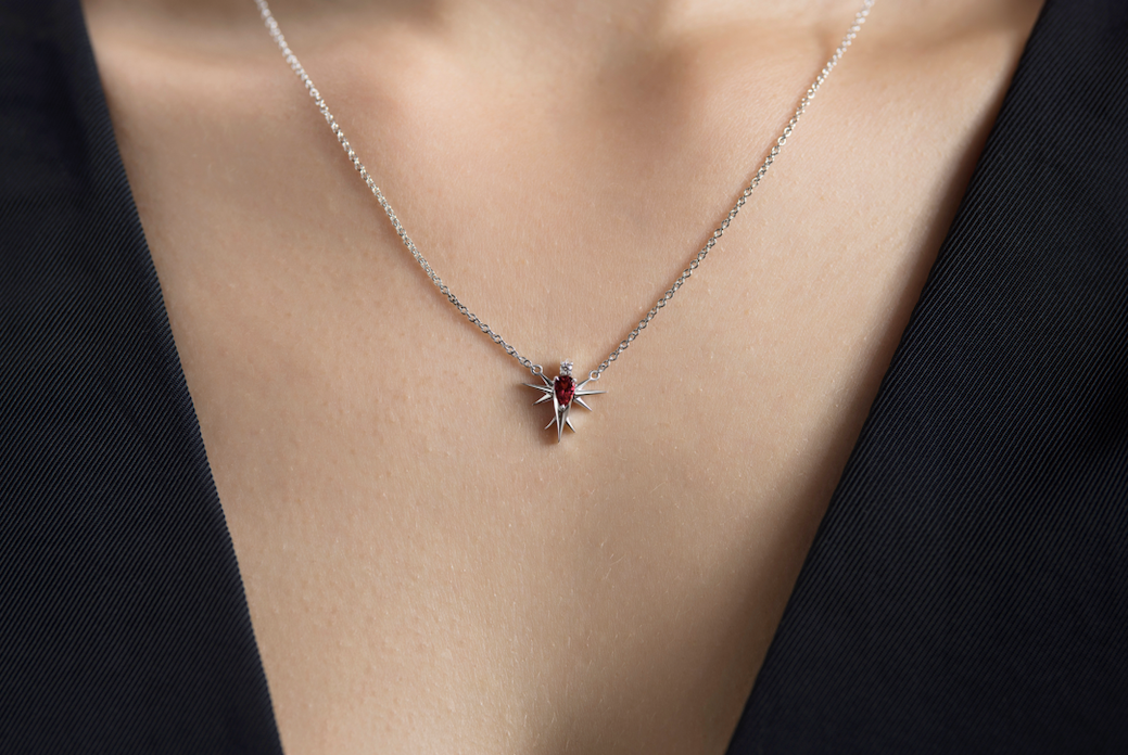 White gold necklace with a pink tourmaline gem bird shaped pendant on a person's neck against a black top.