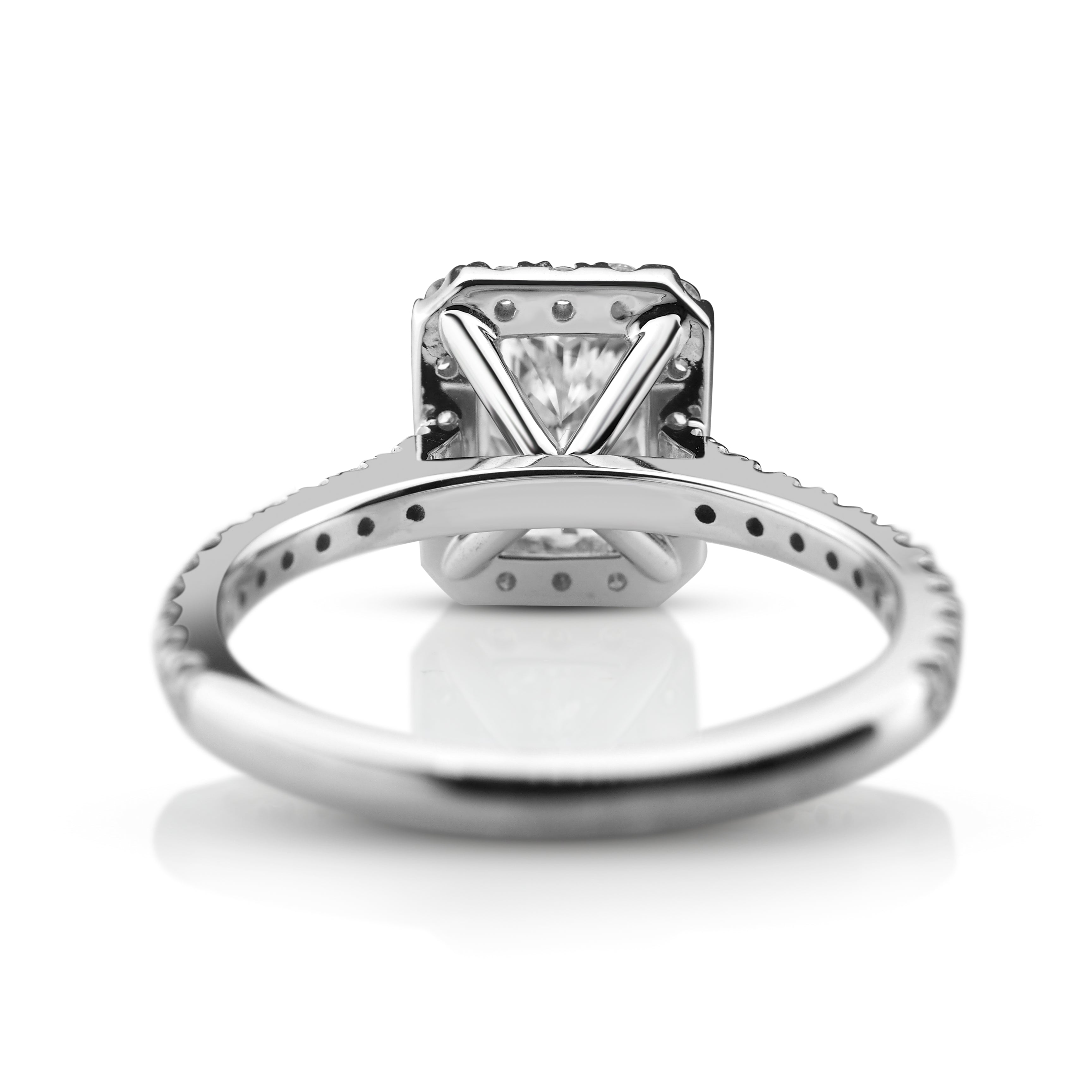 Back view of white gold ring with a radiant cut diamond, showcased on a reflective surface.