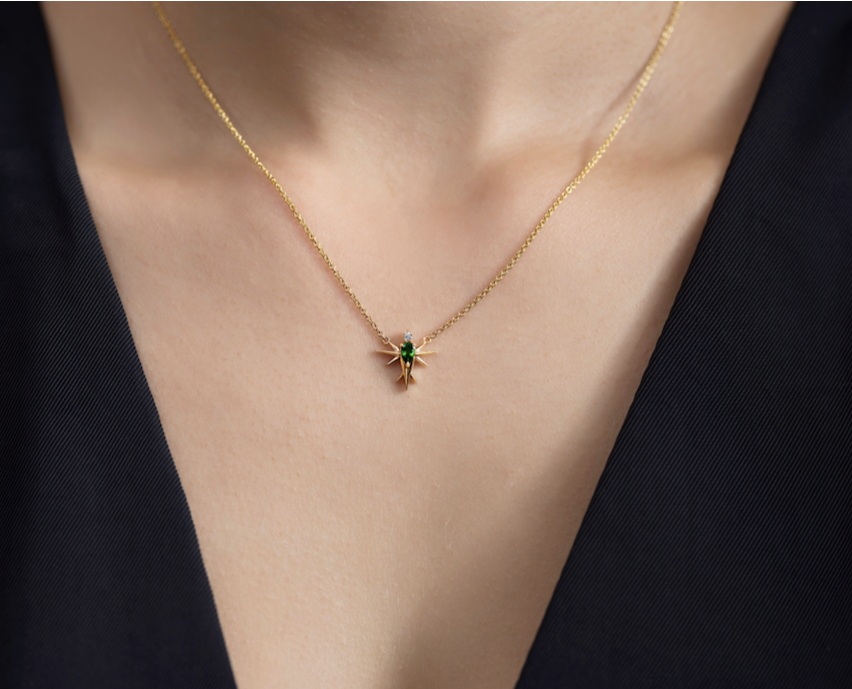 Gold necklace with green Tsavorite gem stone bird pendant on a person's neck against a dark top.