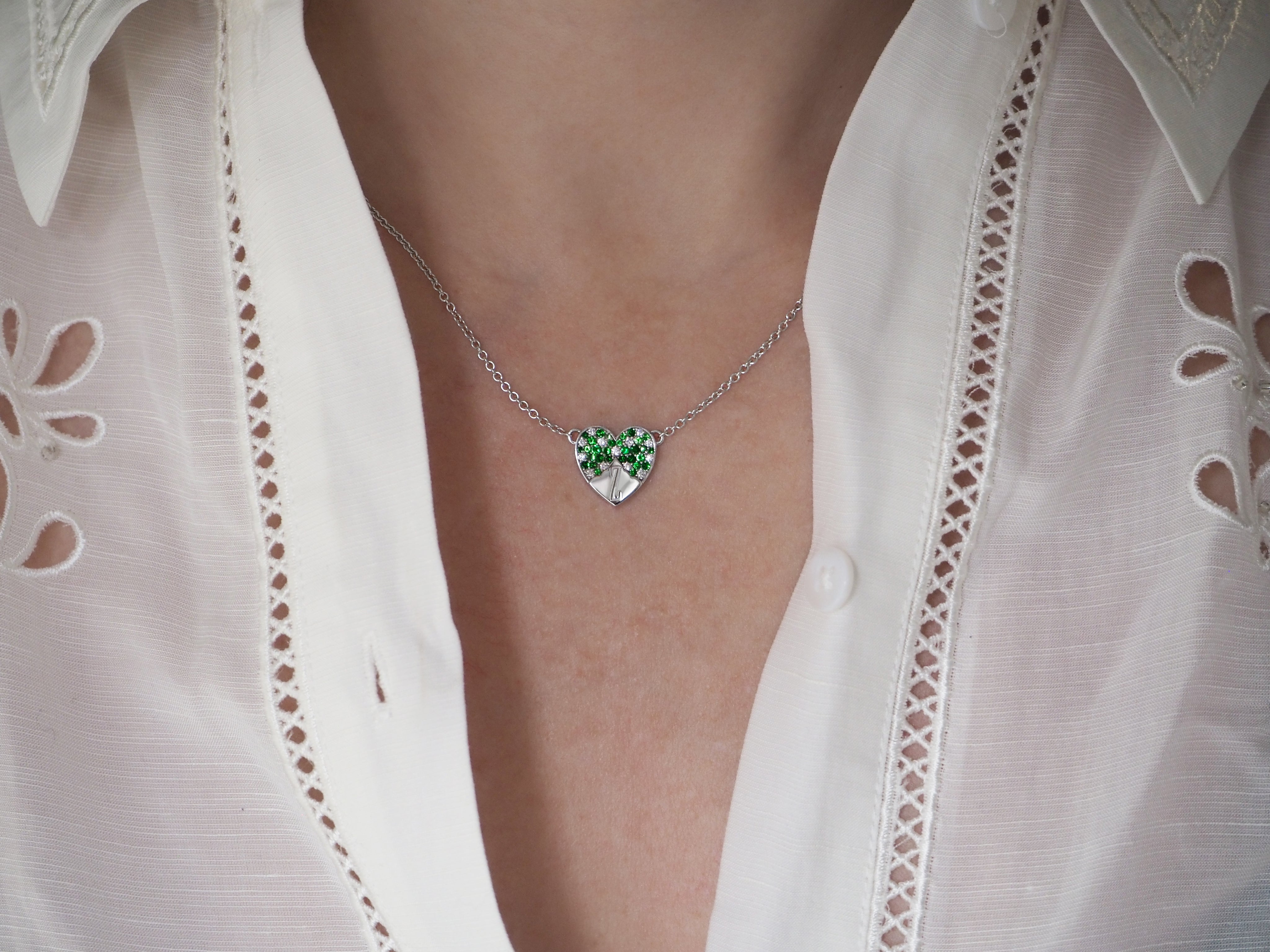 A silver necklace with a heart-shaped pendant featuring green gemstones worn with a white blouse.