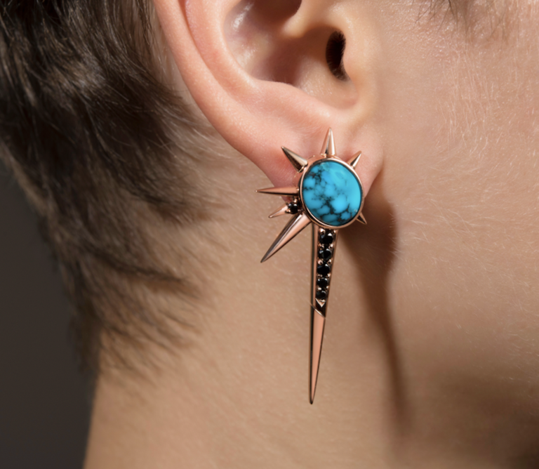 Close-up of a stylish large star shed drop earring with turquoise stone and black diamonds on a person's ear.