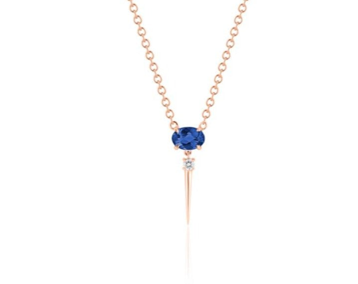 Front view of blue sapphire drop necklace. A horizontal oval-shaped blue sapphire is fixed with 4 prongs to a rose gold round-link chain. Below this, a single link connects to a small round diamond with a dramatic rose gold spike dropping down.