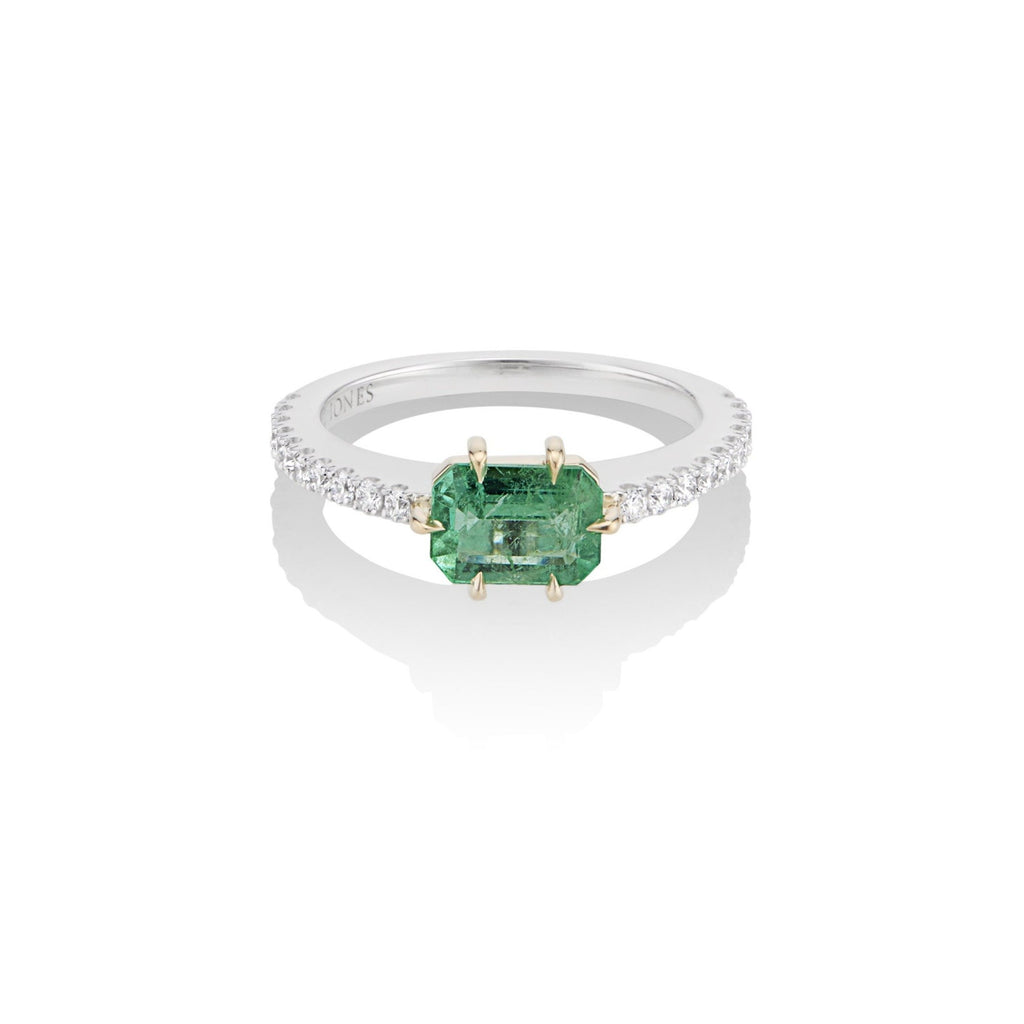 Top view of alternative emerald and diamond engagement ring. The emerald center stone is fixed with a yellow gold 6-prong setting, and mounted atop a U-cut diamond pave band in white gold. The interior band engraving reads, “Harlin Jones.”