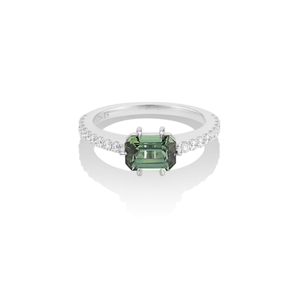 Top view of alternative tourmaline and diamond engagement ring. The green tourmaline center stone is fixed with a rose gold 6-prong setting, and mounted atop a U-cut diamond pave band in white gold. The interior band engraving reads, “Harlin Jones.” 