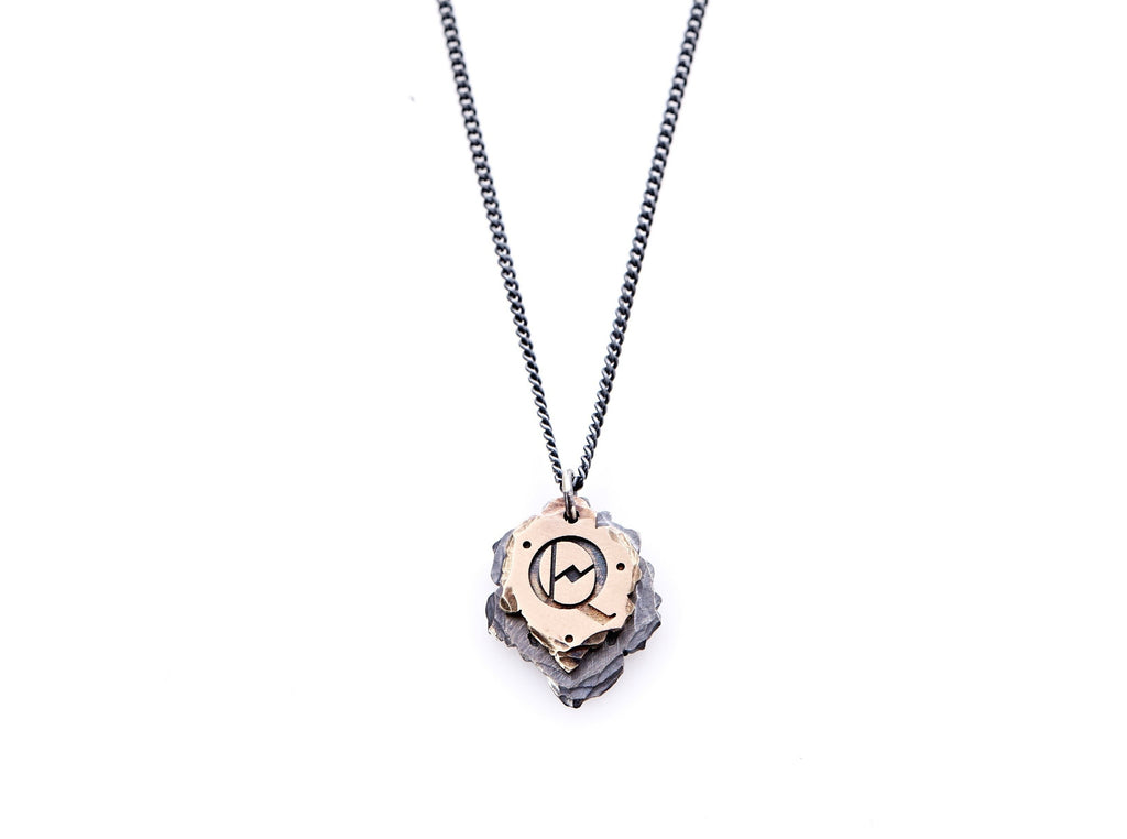 Hand crafted, customizable Initial Necklace with 2 jagged-edged plates hanging from an oxidized sterling silver curbed chain. Top plate is hand forged rose gold with a custom engraving of the letter "Q" in Old English lettering with 2 hand engraved dots on either side. Bottom plate is hand forged oxidized sterling silver and slightly larger than the rose gold plate. The top plate partially covers the bottom plate, and edges of cross- bones are visible on the bottom plate.