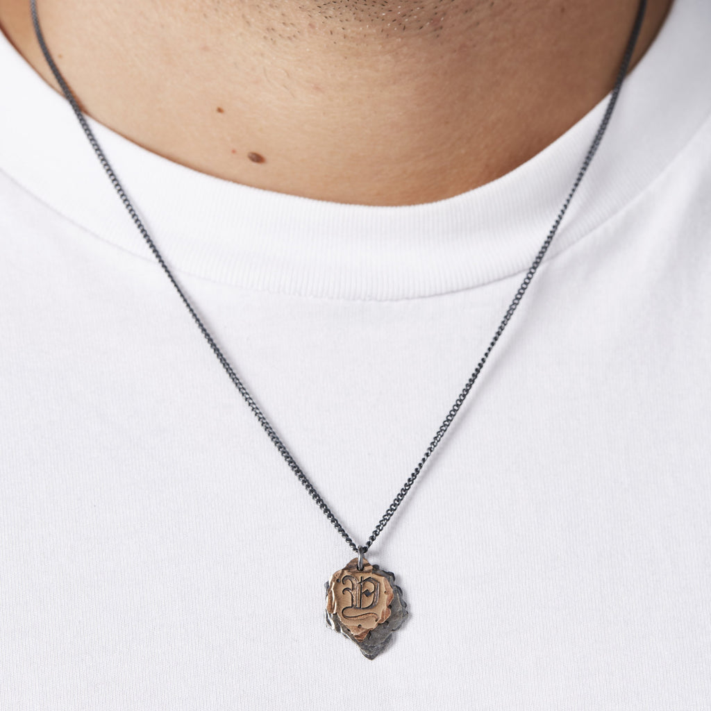 Closeup of a person wearing a bespoke New York jewelry piece, the Initial Necklace, with an engraved letter “Y” in ornate Old English lettering on the rose gold plate. The top plate is dime-sized, and the bottom plate is nickel-sized. The pendant rests at the sternum.