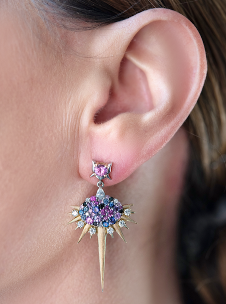  Closeup on an ear wearing the Harlin Jones mixed color sapphire drop earring. The stud fits snugly against the earlobe with the earring’s drop extending down to mid- chin height.