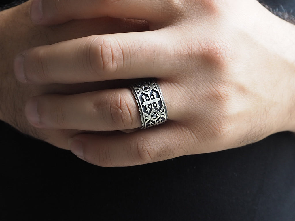 op view of black diamond men’s wedding band worn on the ring finger. The ring fits just below the knuckle, width reaching half-way between the knuckle and base of the finger. The black diamond provides a subtle embellishment within the pattern.