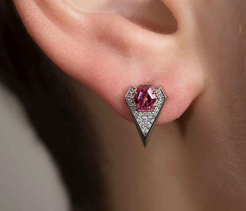 Close-up of an ear with a pink gemstone earring in a triangular silver setting.
