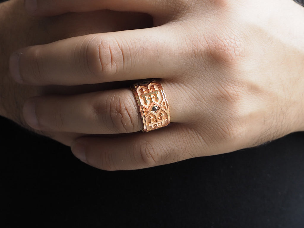 Top view of black diamond men’s wedding band worn on the ring finger. The ring fits just below the knuckle, width reaching half-way between the knuckle and base of the finger. The black diamond provides a subtle embellishment within the pattern.