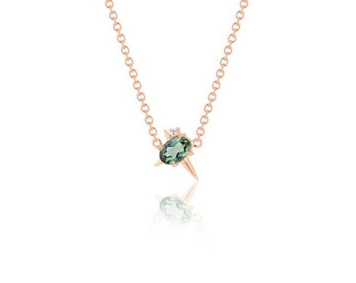  Front view of pendant necklace featuring an oval-shaped green tourmaline gemstone with small round diamond fixed to a rose gold round-link chain. 2 short spikes extend from top and side with a larger spike angled down, creating an angled crucifix.