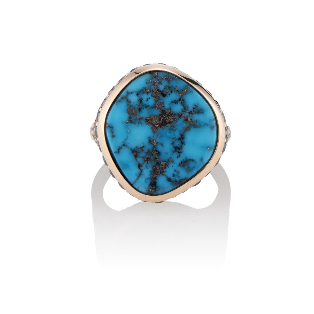 Top view. Bespoke rose gold ring with a large, irregular turquoise stone in a freeform circular-shape rose gold setting. The stone has dark spider-web veins dispersed throughout, with flecks of gold, complimenting the polished rose gold setting.
