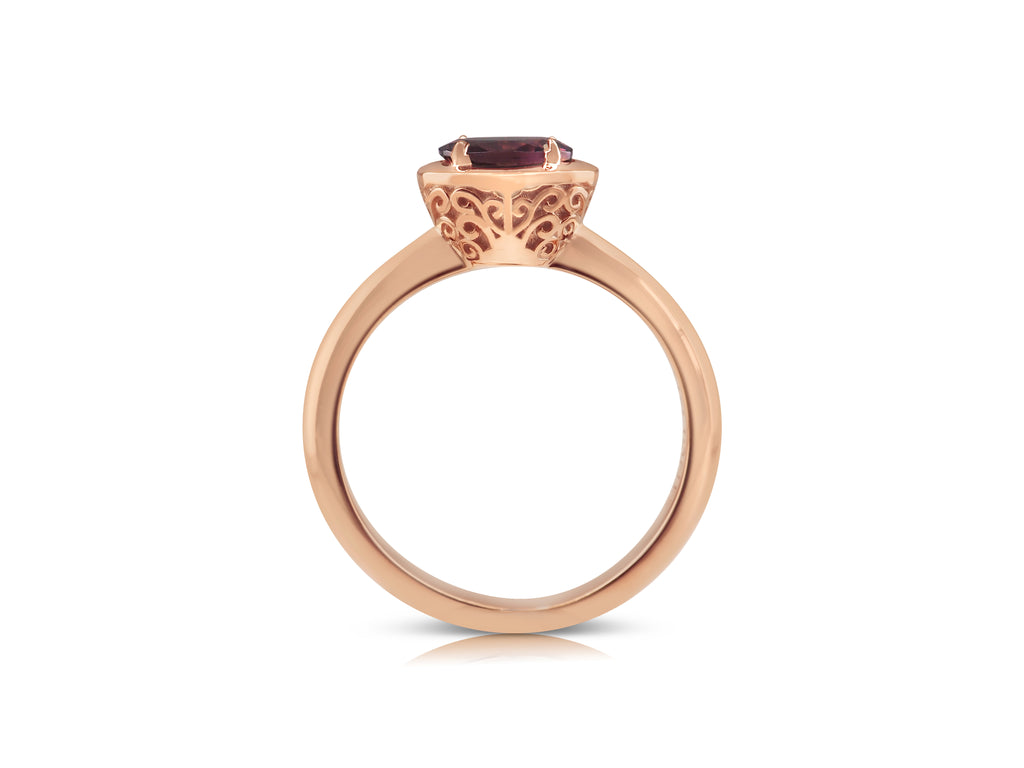 Side view of filigree ring with distinctive rose gold basket. The filigree is a mirrored swirling pattern that reaches up and out from the base of the basket at the bridge. The pink tourmaline stone lays flat, slightly raised above the basket.