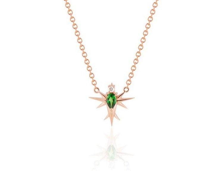 Front view of abstract bird pendant necklace connected to a rose gold round-link chain. A pear-shaped tsavorite stone forms the bird’s body, topped with a round diamond head. Rose gold spikes extend from the body to form wings and a tail. 