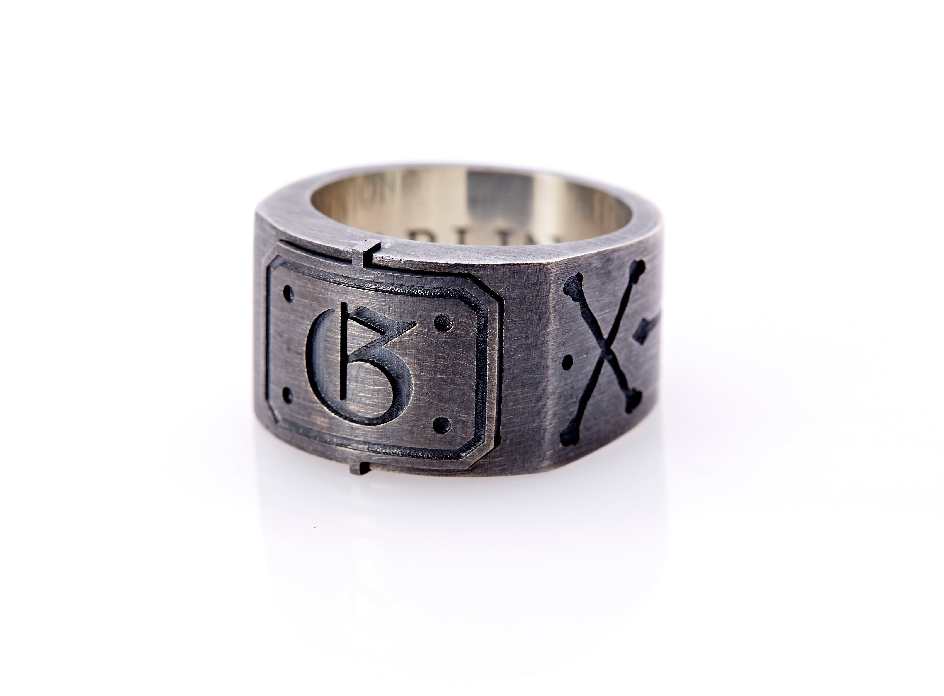 Oxidized sterling silver men’s signet ring with a thick flat band hand-crafted in New York. Semi-raised octagonal engraved top cap with a customizable insignia design of an engraved letter “G” in Old English Style lettering and 4 engraved dots at each corner. The initial on the ring is surrounded by a bold black engraved border that follows the inside edge of the rectangle. The rectangle’s top and bottom edge is accented by a small lip in the center that wraps around the corner edge of the ring.