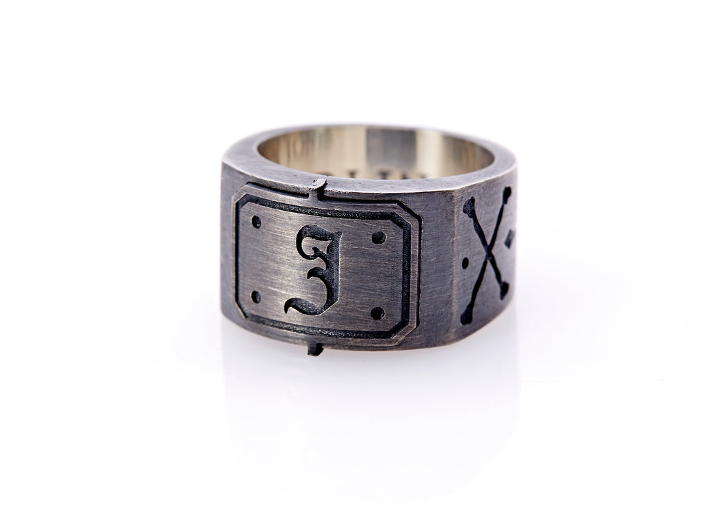 Oxidized sterling silver men’s signet ring with a thick flat band hand-crafted in New York. Semi-raised octagonal engraved top cap with a customizable insignia design of an engraved letter “J” in Old English Style lettering and 4 engraved dots at each corner. The initial on the ring is surrounded by a bold black engraved border that follows the inside edge of the rectangle. The rectangle’s top and bottom edge is accented by a small lip in the center that wraps around the corner edge of the ring.