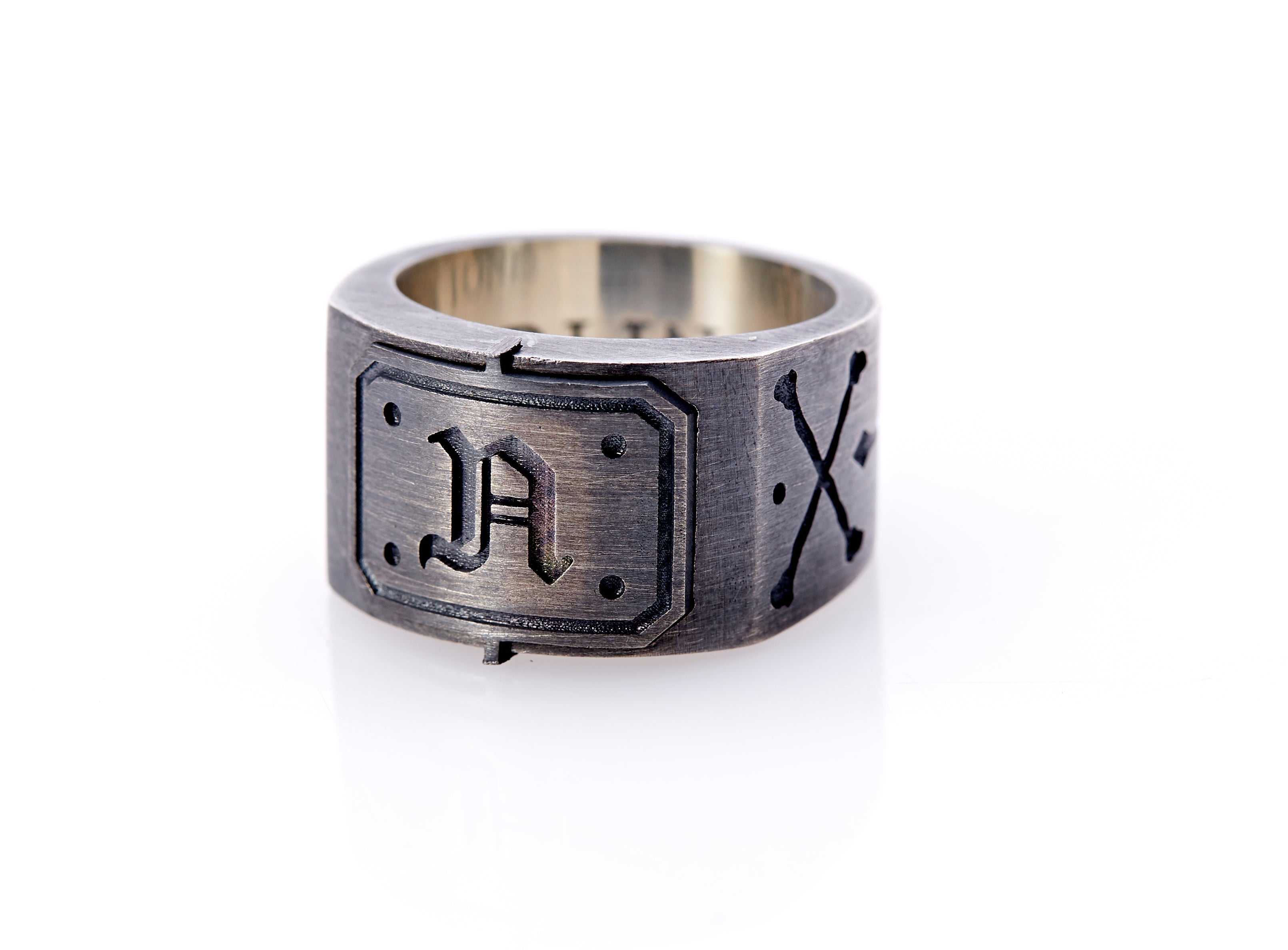 Oxidized sterling silver men’s signet ring with a thick flat band hand-crafted in New York. Semi-raised octagonal engraved top cap with a customizable insignia design of an engraved letter “N” in Old English Style lettering and 4 engraved dots at each corner. The initial on the ring is surrounded by a bold black engraved border that follows the inside edge of the rectangle. The rectangle’s top and bottom edge is accented by a small lip in the center that wraps around the corner edge of the ring.