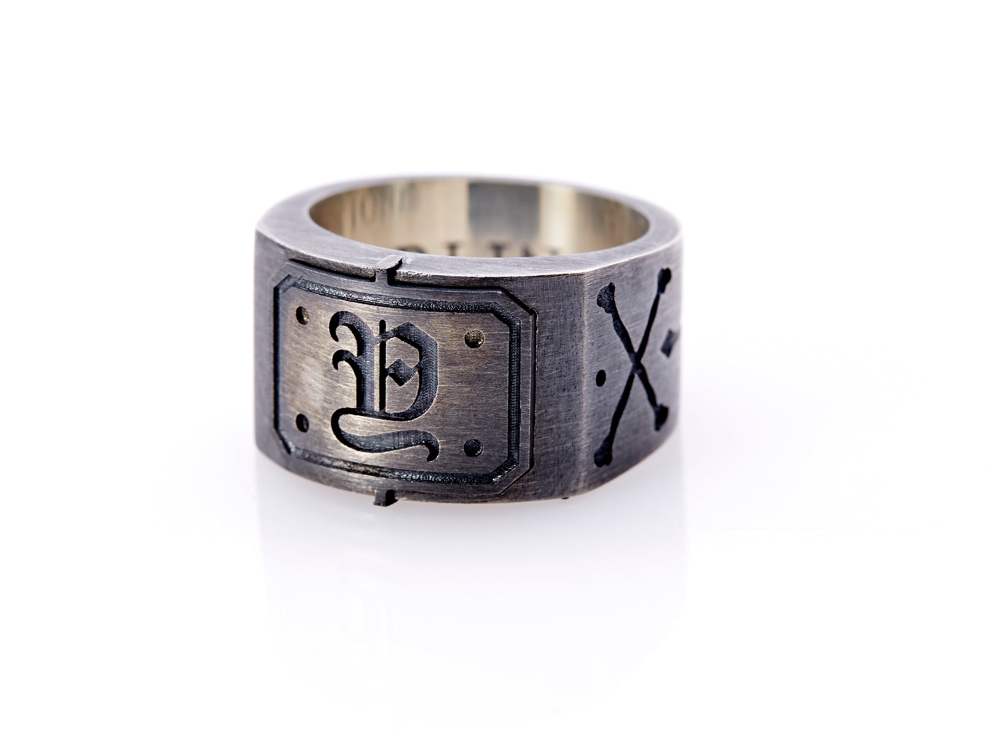 Oxidized sterling silver men’s signet ring with a thick flat band hand-crafted in New York. Semi-raised octagonal engraved top cap with a customizable insignia design of an engraved letter “Y” in Old English Style lettering and 4 engraved dots at each corner. The initial on the ring is surrounded by a bold black engraved border that follows the inside edge of the rectangle. The rectangle’s top and bottom edge is accented by a small lip in the center that wraps around the corner edge of the ring.