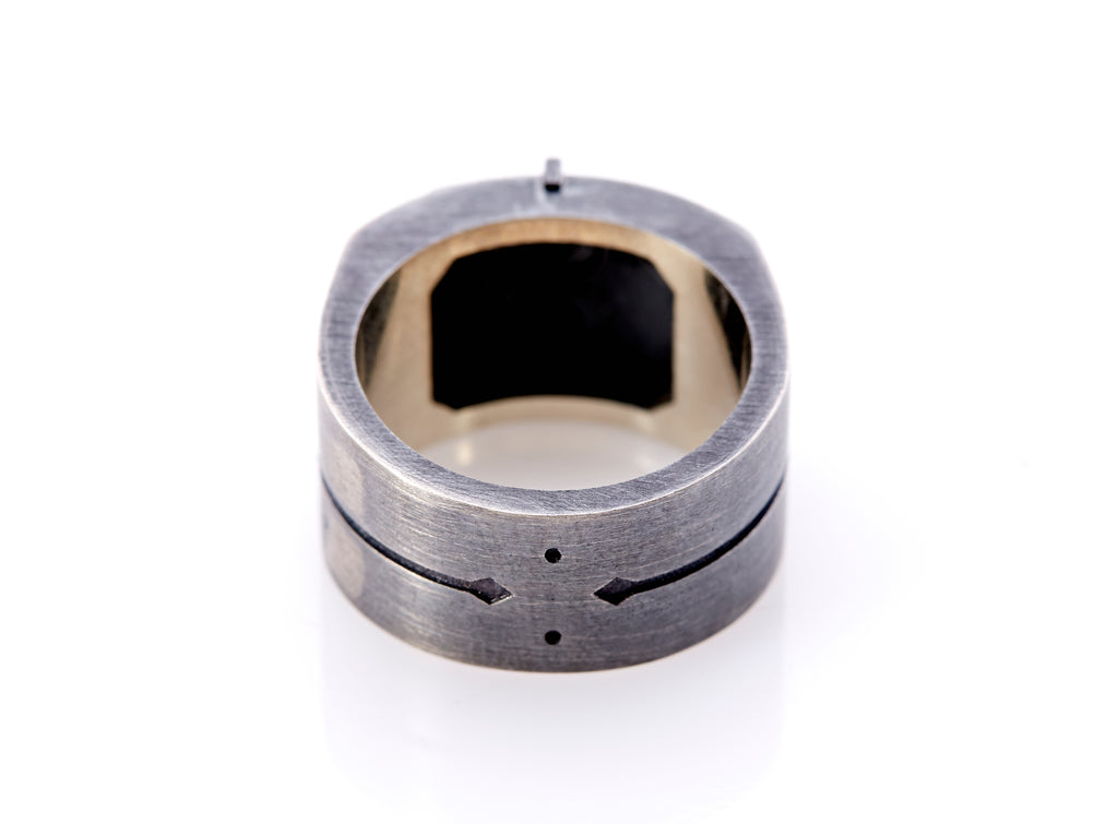 Base of signet ring with details of arrows and dots. The oxidized silver has a brushed finish. Inner band of the ring’s top is visible which has an octagonal square for the ring's insignia.
