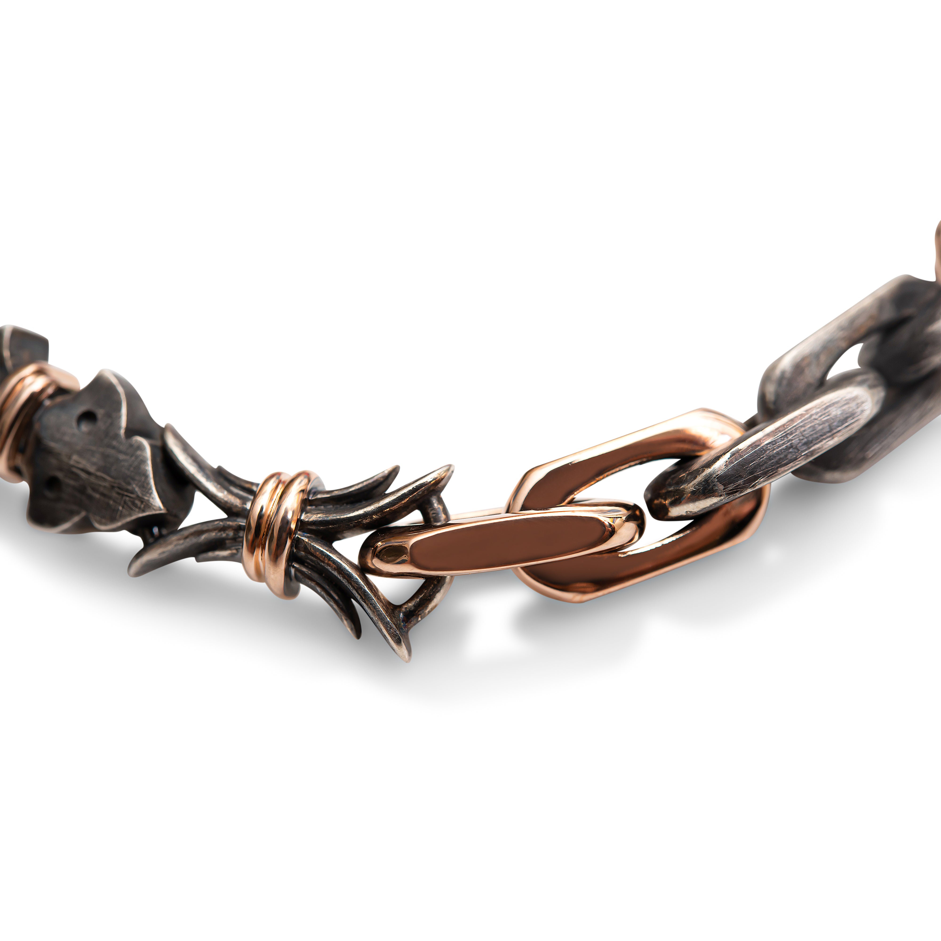 Closeup on link details for oxidized sterling silver and rose gold bracelet. The abstract bowtie has a rose gold binding around the center. This double link is connected to a rose gold elongated link which leads to another rose gold elongated link. This link is connected to an oxidized sterling silver link, which leads to 2 more sterling silver links. The rose gold pieces have a smooth, polished texture and lustrous appearance. The oxidized sterling silver pieces have a grainy texture and muted appearance.