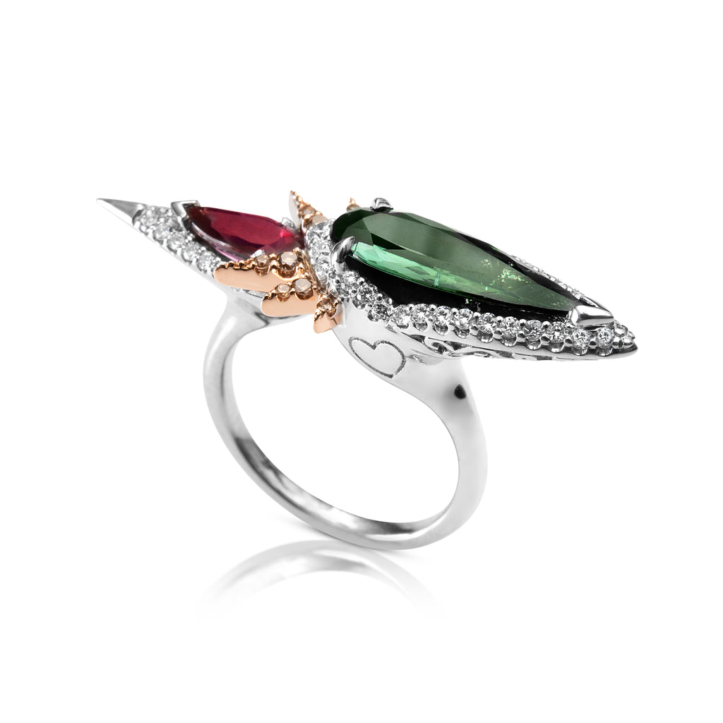  Partial side angle of the Tourmaline Diamond Ring. The thin white gold band is joined together at the center, curving up to a point and showing the heart shaped detailing below the green tourmaline gem. The shoulders are asymmetrical with the thicker shoulder with the heart engraving below the green tourmaline gem.