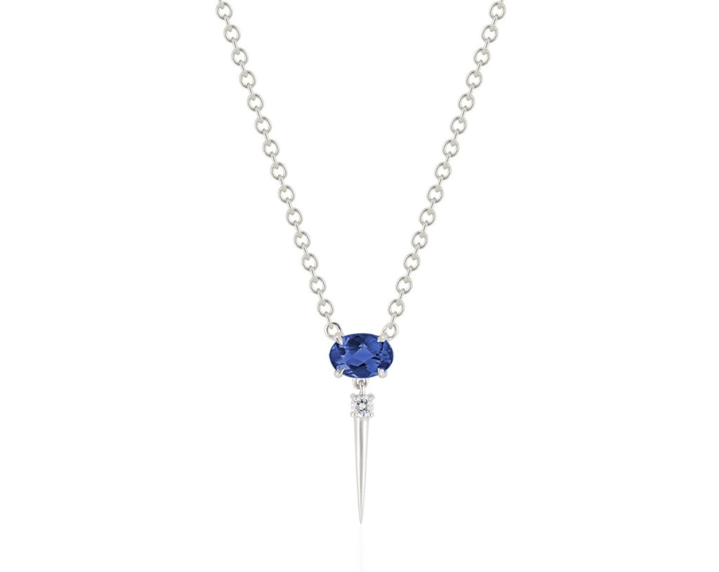 Front view of blue sapphire drop necklace. A horizontal oval-shaped blue sapphire is fixed with 4 prongs to a white gold round-link chain. Below this, a single link connects to a small round diamond with a dramatic white gold spike dropping down.