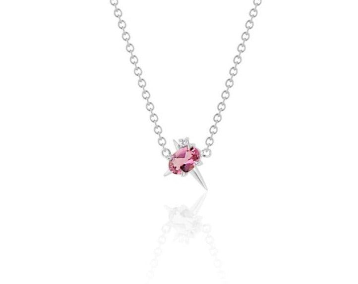 Front view of pendant necklace featuring an oval-shaped pink tourmaline gemstone with small round diamond fixed to a white gold round-link chain. 2 short spikes extend from top and side with a larger spike angled down, creating an angled crucifix.
