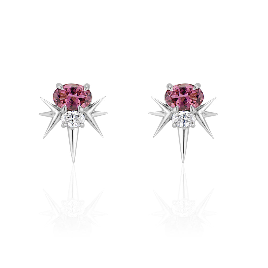  Front view of white gold spike earrings, each featuring 1 horizontal oval-shaped pink tourmaline stone with 1 oval-shaped diamond below. 7 white gold spikes extend out from the diamond, 3 on either side and 1 slightly longer spike pointed down. 