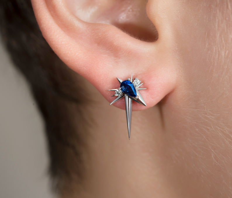 Close-up of an ear with a star-shaped earring featuring a blue gem and silver spikes.