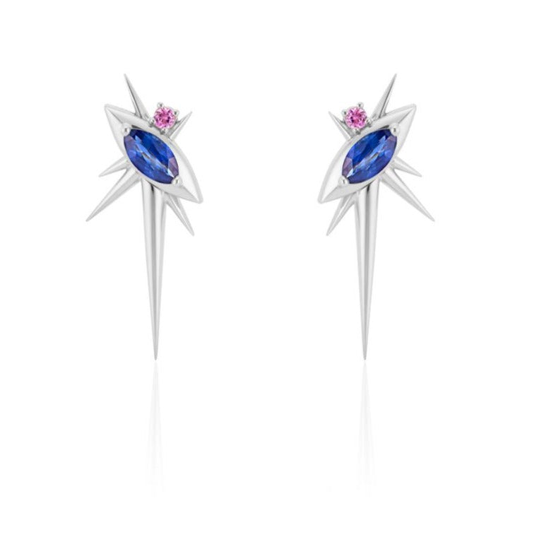 Front view of alternative drop earrings, each with 1 marquise-shaped blue sapphire, set at a 45-degree angle, with a small pink sapphire above. 6 white gold spikes of varying lengths extend from the setting, with a large, long spike pointed down. 