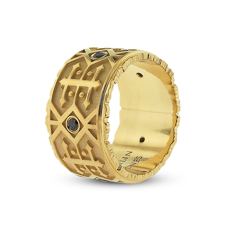Front side angle of black diamond men’s wedding band. Polished yellow gold detailing features alternating navajo-style designs; a grid of double-sided arrows with dots, and 2 rows of side-by-side zig-zag lines with centered round black diamond.