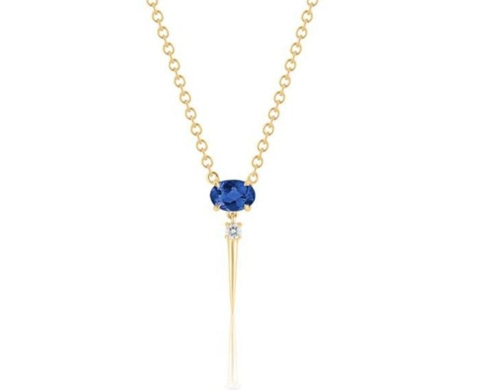 Front view of blue sapphire drop necklace. A horizontal oval-shaped blue sapphire is fixed with 4 prongs to a yellow gold round-link chain. Below this, a single link connects to a small round diamond with a dramatic yellow gold spike dropping down.