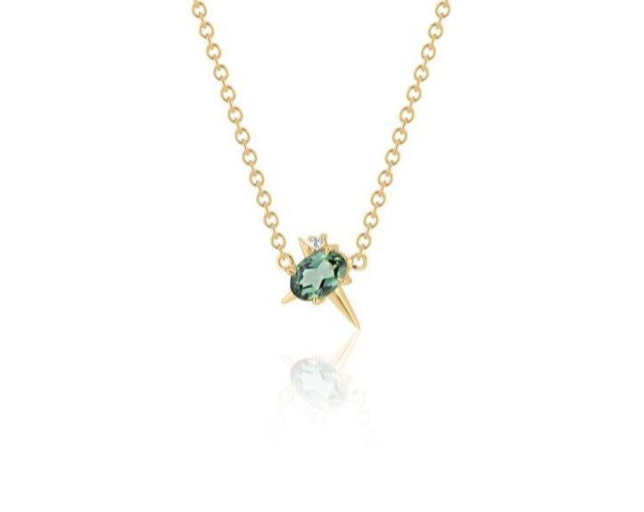  Front view of pendant necklace featuring an oval-shaped green tourmaline gemstone with small round diamond fixed to a yellow gold round-link chain. 2 short spikes extend from top and side with a larger spike angled down, creating an angled crucifix.
