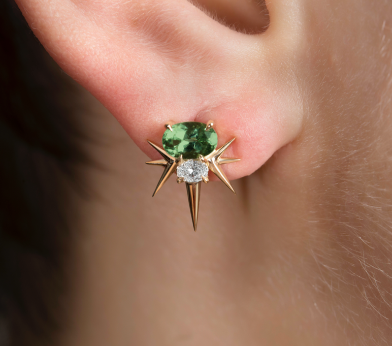 Close-up of an ear with a green gemstone earring accented by spikes and diamonds.