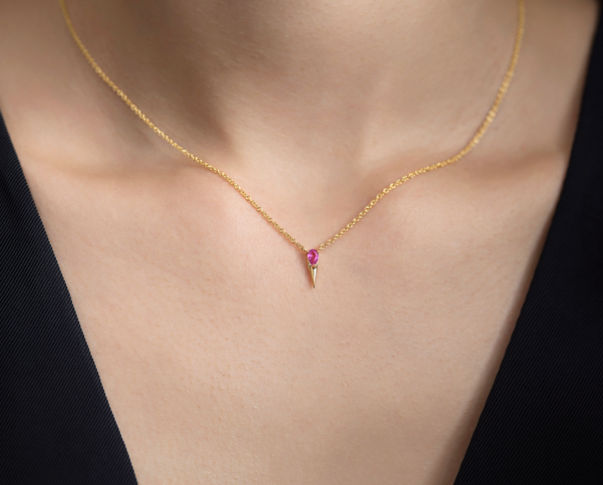 Golden necklace with a single pink gemstone pendant on a person's neck against a black background.
