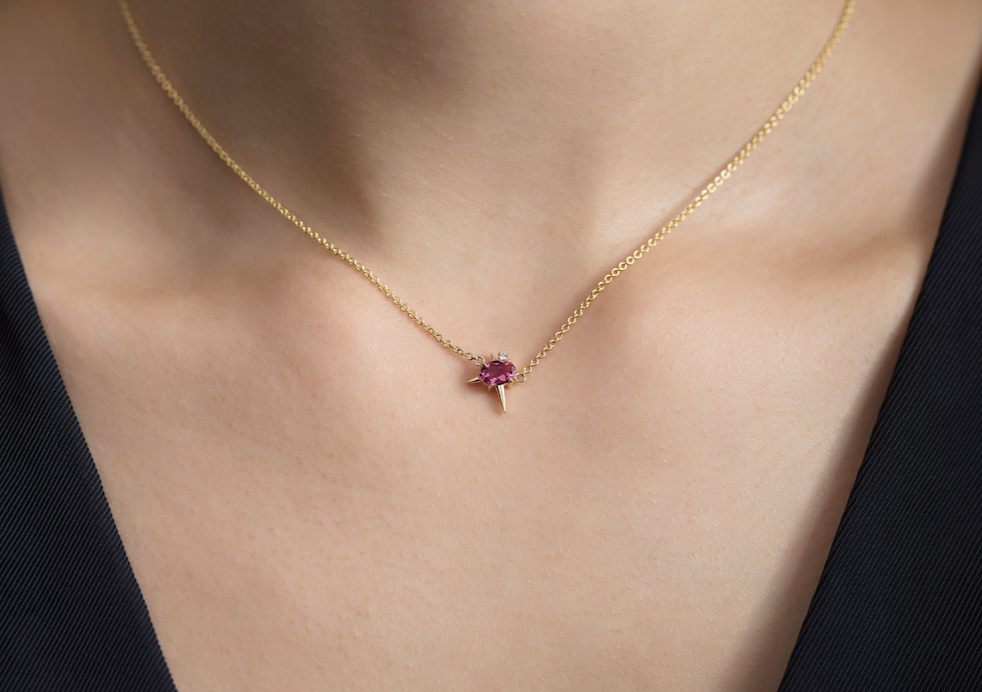 Gold necklace with a pink tourmaline and diamond pendant on a person's neck.