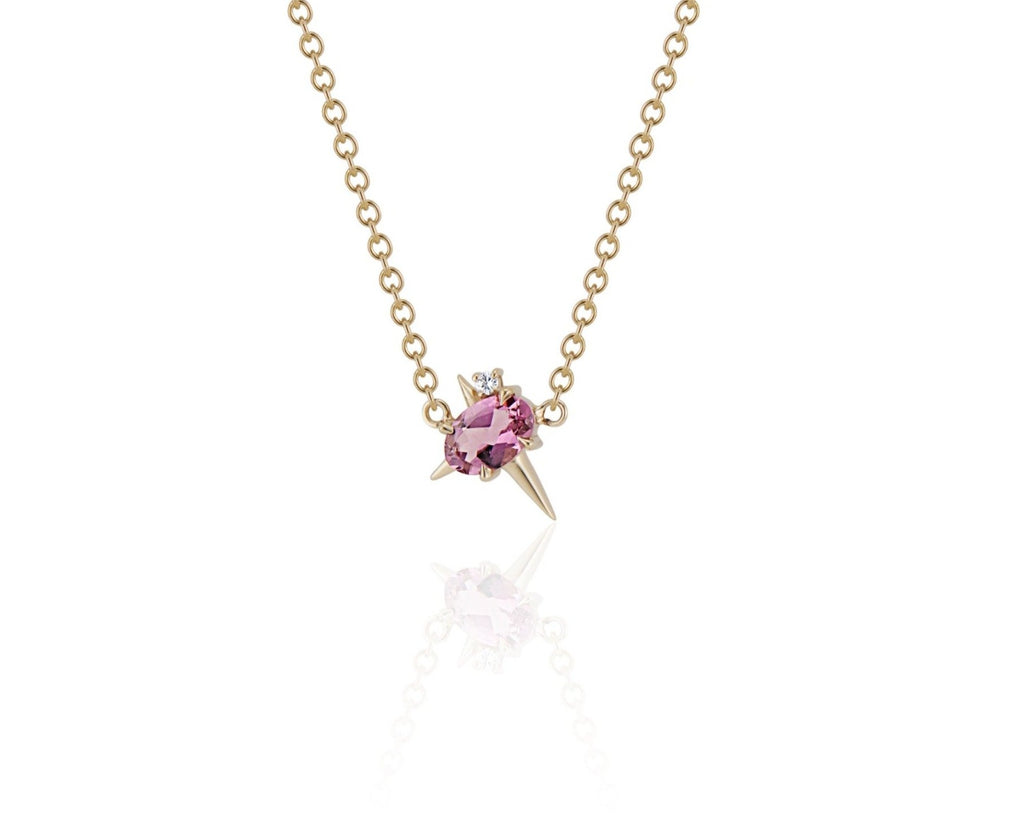 Front view of pendant necklace featuring an oval-shaped pink tourmaline gemstone with small round diamond fixed to a yellow gold round-link chain. 2 short spikes extend from top and side with a larger spike angled down, creating an angled crucifix.