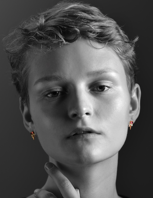 Person from behind with a finger on lips, earring visible, on a black background.