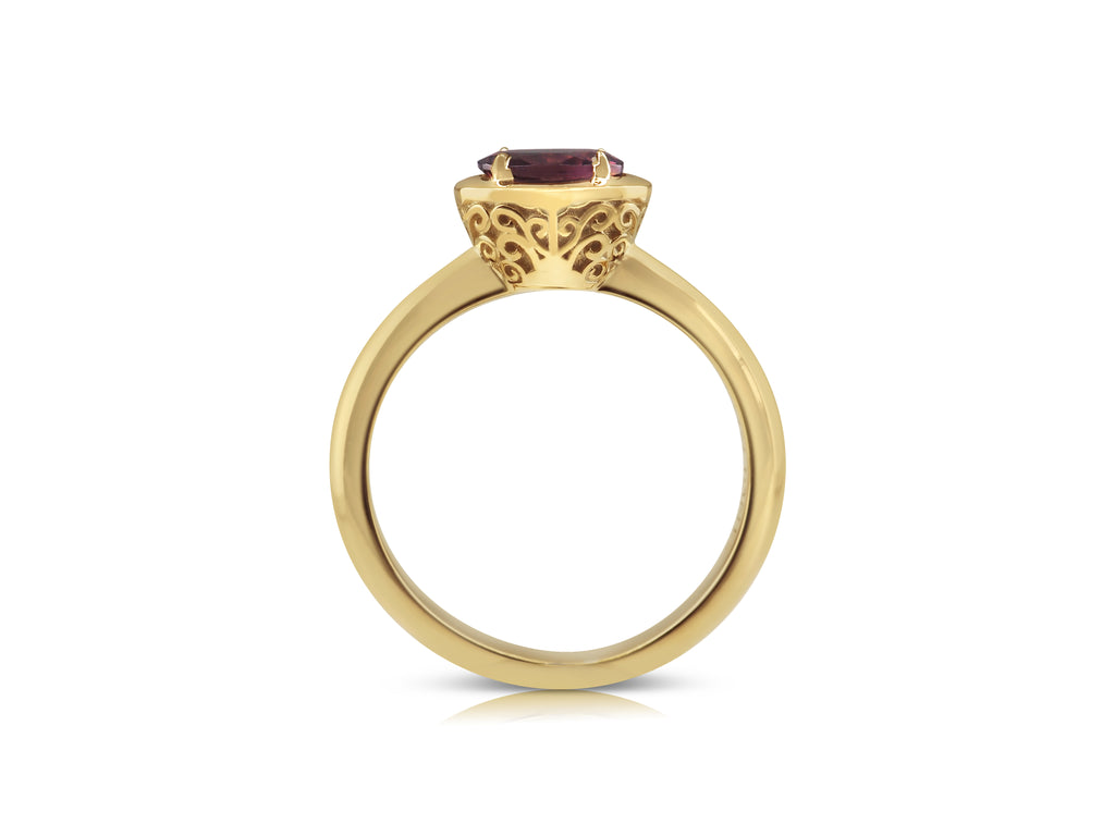 Side view of filigree ring with distinctive yellow gold basket. The filigree is a mirrored swirling pattern that reaches up and out from the base of the basket at the bridge. The pink tourmaline stone lays flat, slightly raised above the basket.