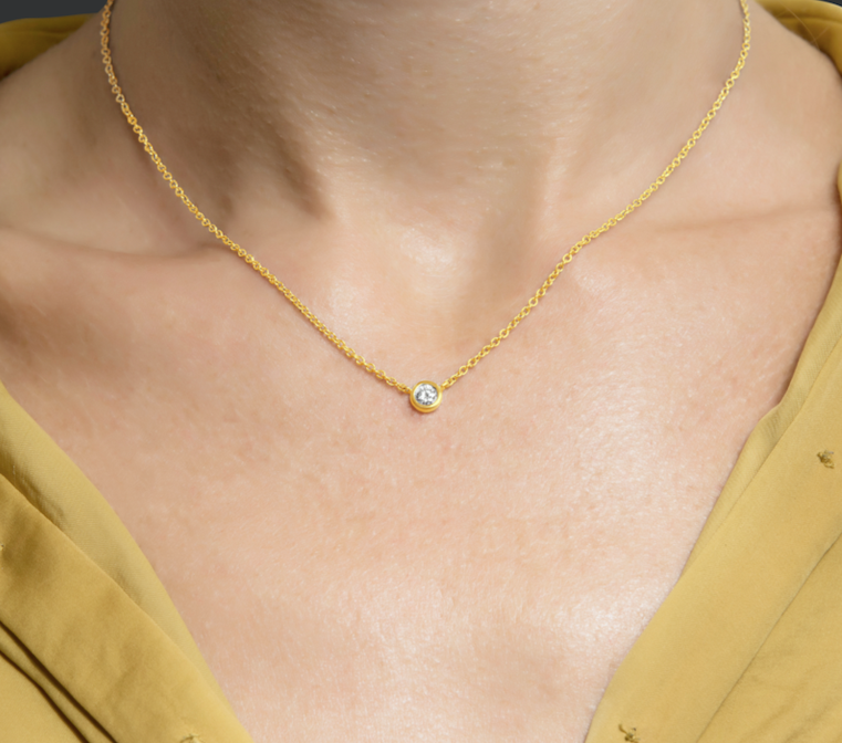 Close-up of a gold necklace with a single diamond pendant on a person's neck.
